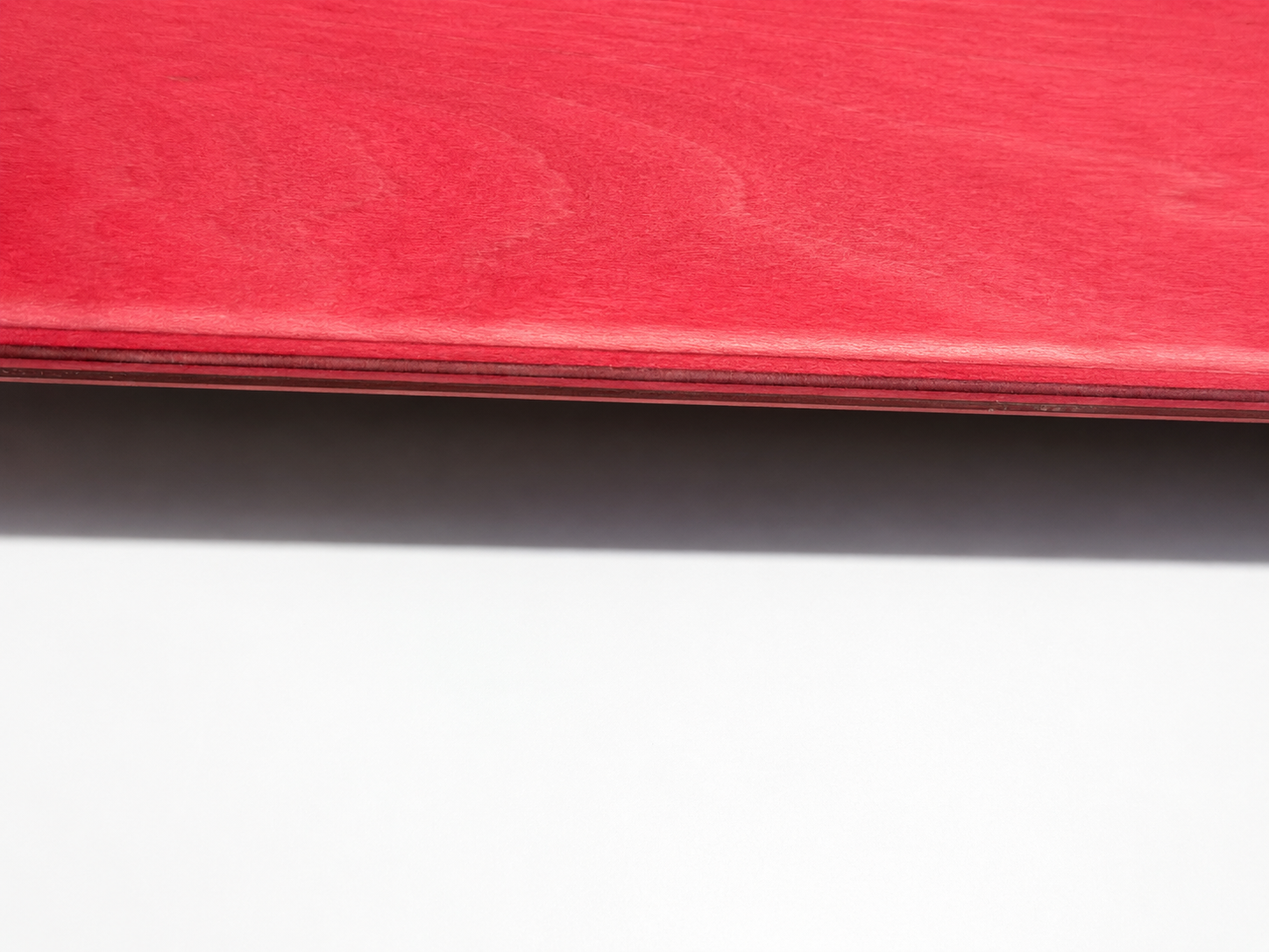 Close-up of an Asinine Skateboards premium skateboard deck showing tightly bonded seven-ply Canadian maple veneers with epoxy resin construction.
