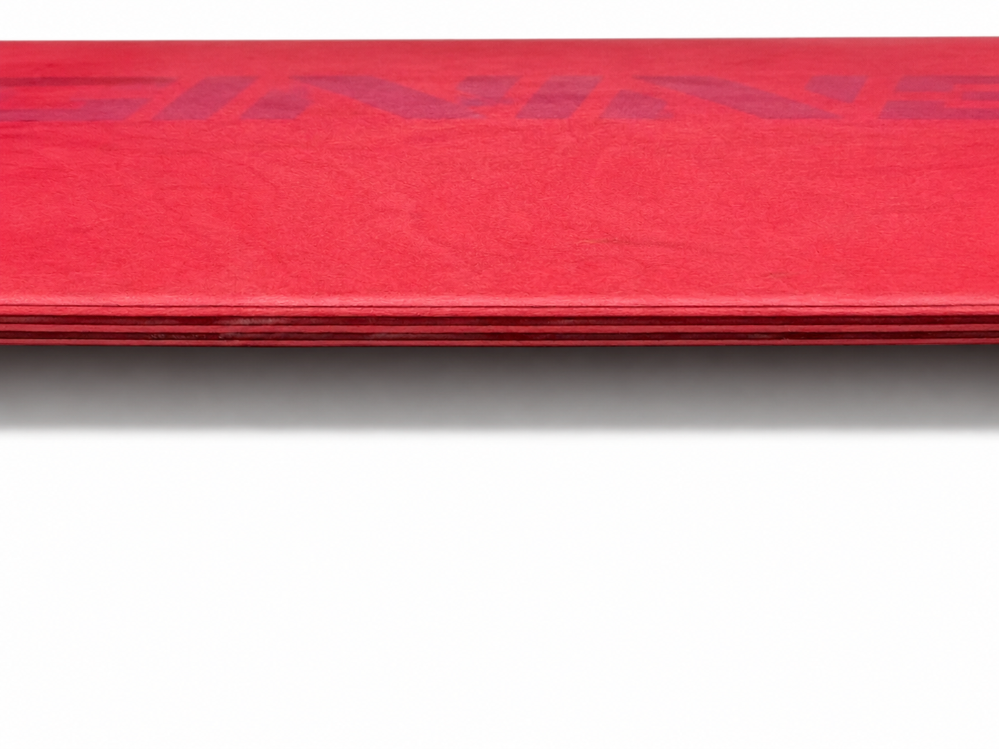 Close-up of the exposed seven-ply Canadian maple veneers along the edge of an Asinine Skateboards deck, showing premium construction.