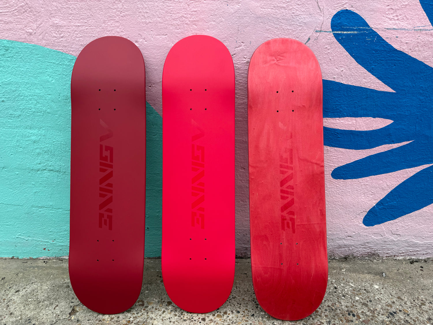 Three premium Asinine skateboard decks with satin finish standing against a colorful mural.