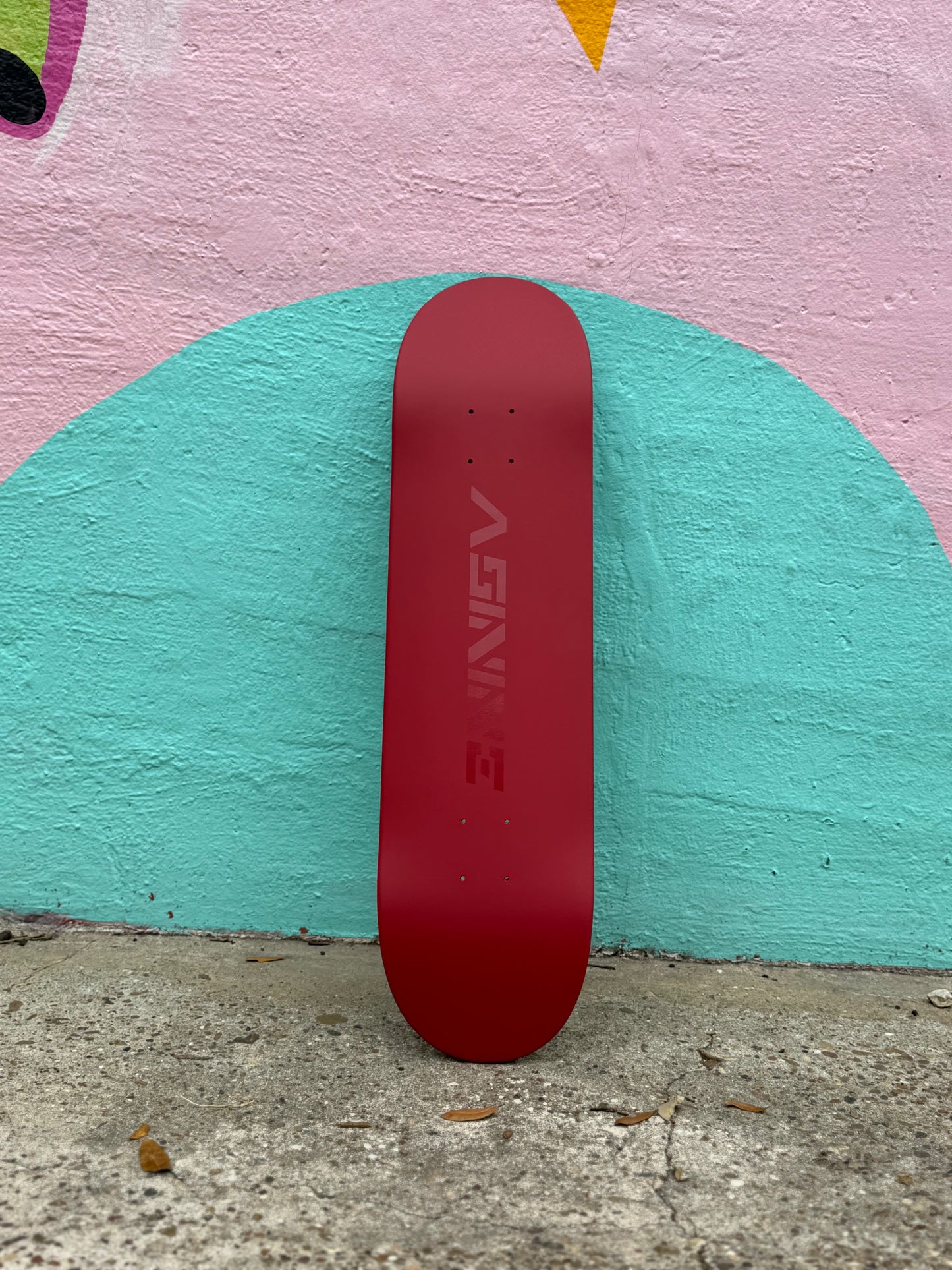 The Classic skateboard deck standing upright against a colorful mural, showcasing the satin red finish and high-gloss logo.